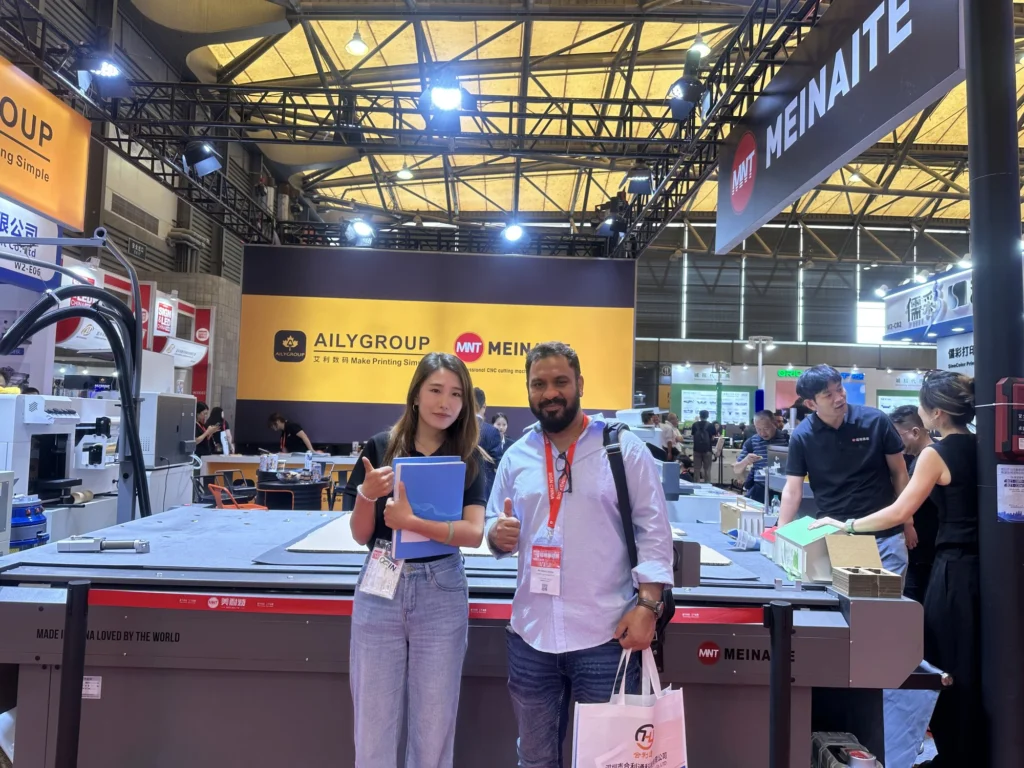Overseas buyers at the MNT MEINAITE stand at SIGN CHINA 2026 beside the C2516T digital cutting table with cut board samples